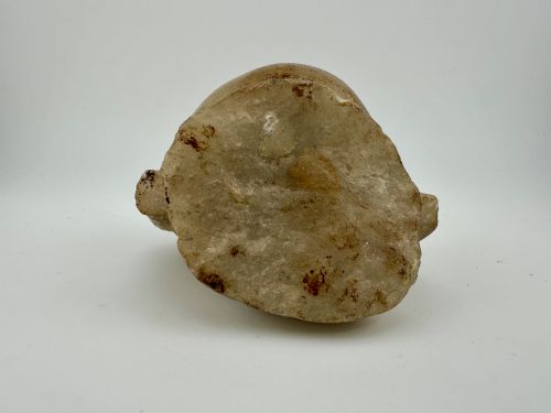 fig 4. A carved off-white hardstone head fragment featuring facial features, elongated earlobes, and faint traces of gilding across the surface.