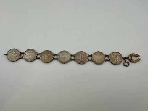 fig 1. A silver-toned metal bracelet made from scalloped 1956 Guernsey threepence coins featuring a cow and coat of arms, connected to a horseshoe charm and bolt ring clasp.