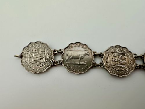 fig 2. A silver-toned metal bracelet made from scalloped 1956 Guernsey threepence coins featuring a cow and coat of arms, connected to a horseshoe charm and bolt ring clasp.