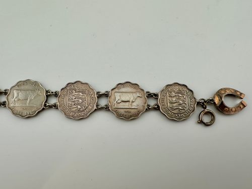 fig 3. A silver-toned metal bracelet made from scalloped 1956 Guernsey threepence coins featuring a cow and coat of arms, connected to a horseshoe charm and bolt ring clasp.