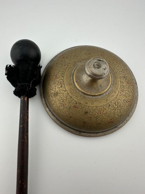 fig 1. An antique domed Indian brass hand gong with detailed floral engravings, a turned central finial handle, and a dark wooden striker.
