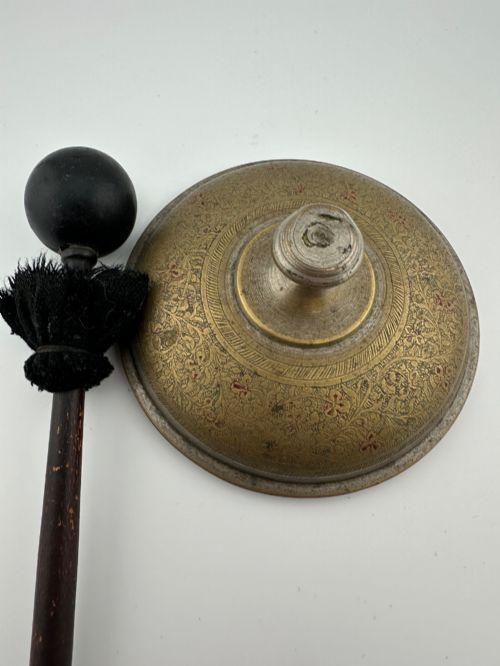 fig 4. An antique domed Indian brass hand gong with detailed floral engravings, a turned central finial handle, and a dark wooden striker.