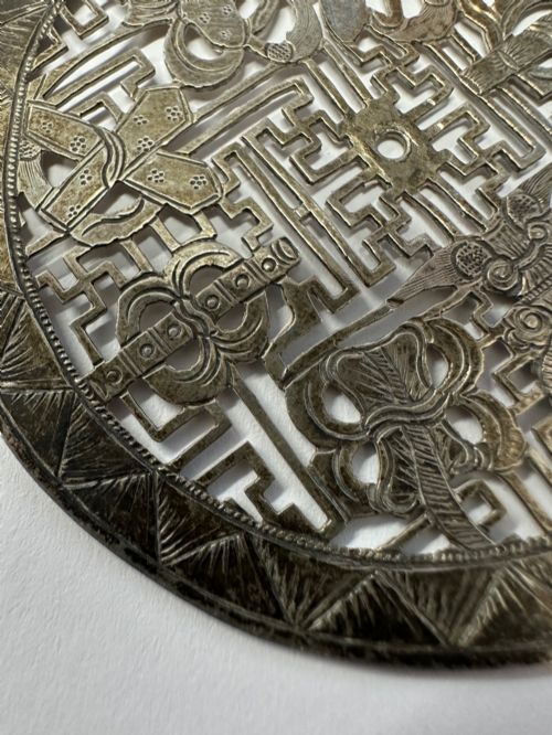 fig 2. A circular 19th-century Tibetan silver plaque featuring openwork fretwork and hand-engraved Buddhist auspicious symbols framed by a geometric border.