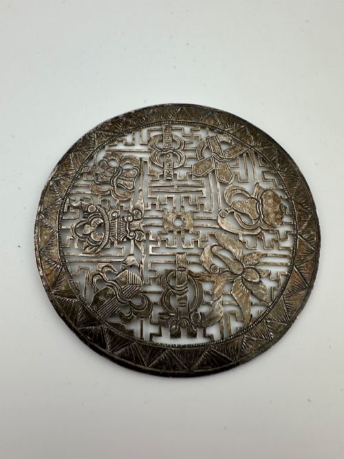 fig 3. A circular 19th-century Tibetan silver plaque featuring openwork fretwork and hand-engraved Buddhist auspicious symbols framed by a geometric border.