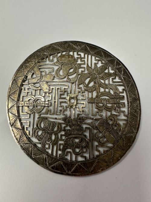 fig 4. A circular 19th-century Tibetan silver plaque featuring openwork fretwork and hand-engraved Buddhist auspicious symbols framed by a geometric border.