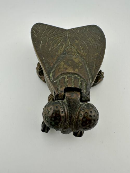fig 1. A cast dark brass match holder sculpted in the detailed shape of a fly with textured wings, compound eyes, and six legs.