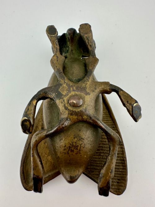 fig 5. A cast dark brass match holder sculpted in the detailed shape of a fly with textured wings, compound eyes, and six legs.