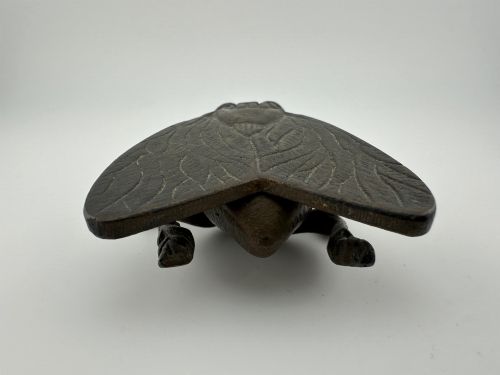 fig 6. A cast dark brass match holder sculpted in the detailed shape of a fly with textured wings, compound eyes, and six legs.