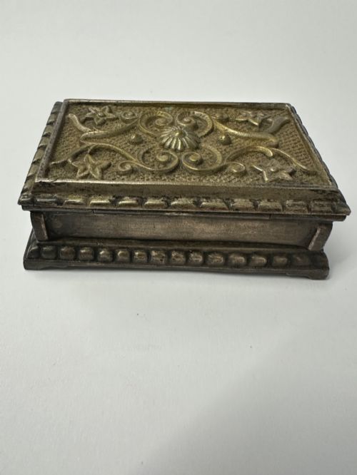 fig 2. An antique silvered brass desktop vesta box with a hinged floral embossed lid, ribbed striker strip, and front tray resting on a beaded base.