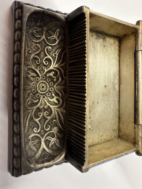 fig 4. An antique silvered brass desktop vesta box with a hinged floral embossed lid, ribbed striker strip, and front tray resting on a beaded base.