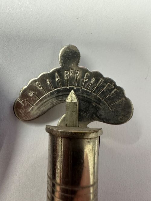 fig 1. A cylindrical nickel-plated chromatic variable pitch pipe with a note scale arc sitting inside its open red metal case.