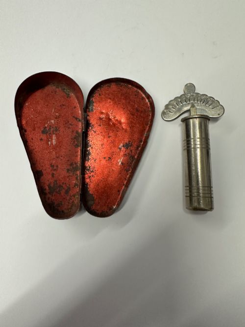 fig 3. A cylindrical nickel-plated chromatic variable pitch pipe with a note scale arc sitting inside its open red metal case.