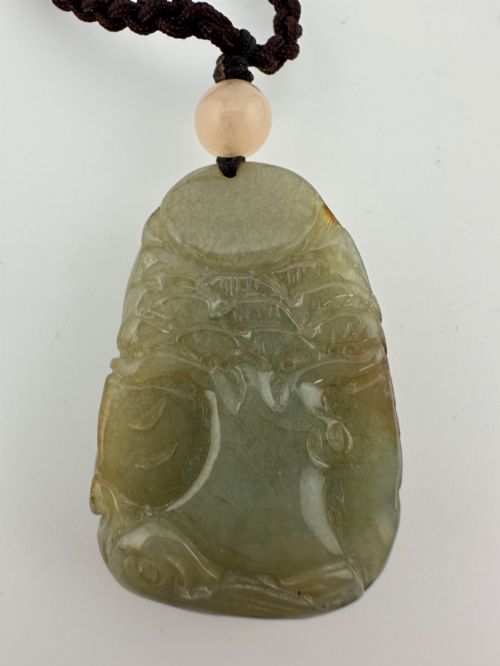 fig 1. A hand-carved yellow and green jade pendant depicting a phoenix among foliage, suspended from a cord with a spherical accent bead.