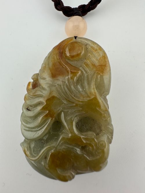 fig 3. A hand-carved yellow and green jade pendant depicting a phoenix among foliage, suspended from a cord with a spherical accent bead.