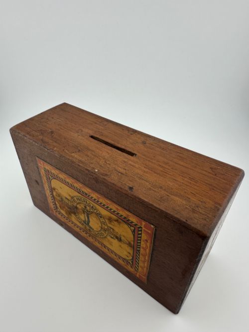 fig 1. A rectangular dark wooden church collection box featuring a coin slot on top and a printed yellow and red Society for the Propagation of the Gospel label on the front.