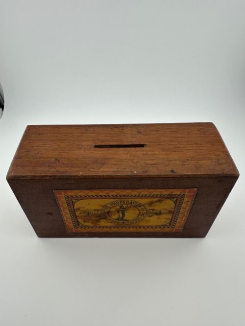 fig 3. A rectangular dark wooden church collection box featuring a coin slot on top and a printed yellow and red Society for the Propagation of the Gospel label on the front.