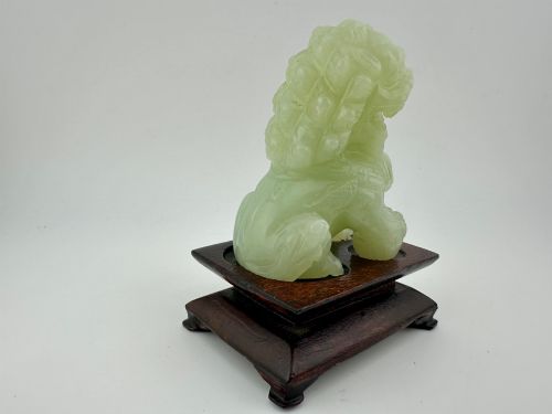 fig 1. A hand-carved pale green jade guardian lion sculpture resting on a dark carved timber base.