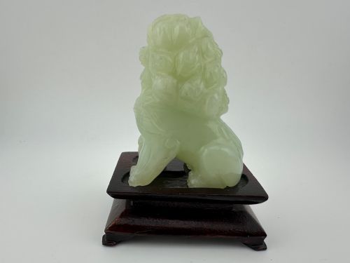 fig 3. A hand-carved pale green jade guardian lion sculpture resting on a dark carved timber base.