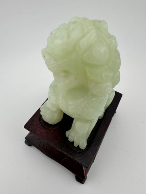 fig 4. A hand-carved pale green jade guardian lion sculpture resting on a dark carved timber base.