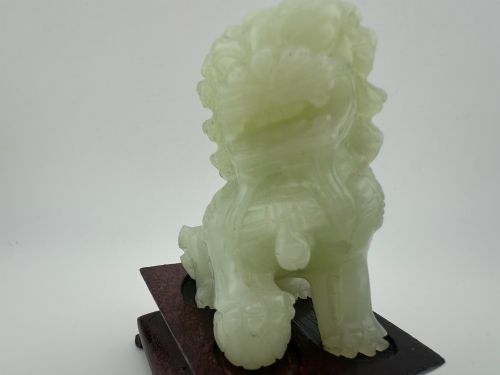 fig 5. A hand-carved pale green jade guardian lion sculpture resting on a dark carved timber base.
