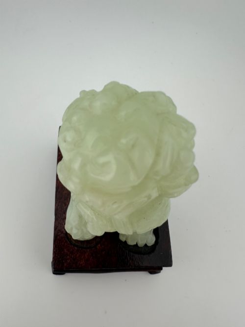 fig 6. A hand-carved pale green jade guardian lion sculpture resting on a dark carved timber base.