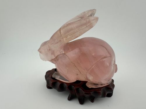 fig 2. A hand-carved pink rose quartz rabbit figurine with upright ears seated on a dark fitted hardwood display base.