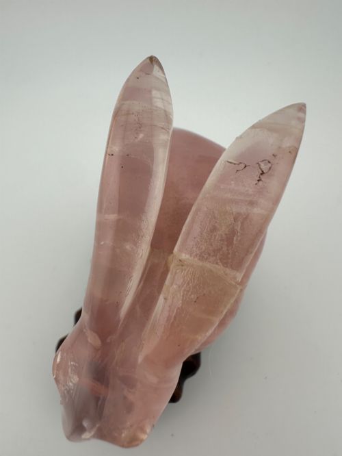 fig 3. A hand-carved pink rose quartz rabbit figurine with upright ears seated on a dark fitted hardwood display base.