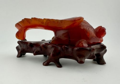 fig 1. A translucent terracotta orange carnelian agate sculpture of a fantail goldfish positioned on a carved dark brown hardwood stand.