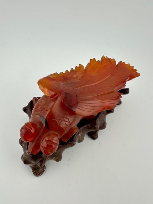 fig 2. A translucent terracotta orange carnelian agate sculpture of a fantail goldfish positioned on a carved dark brown hardwood stand.