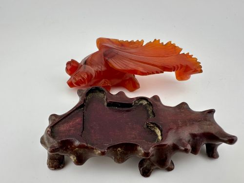 fig 5. A translucent terracotta orange carnelian agate sculpture of a fantail goldfish positioned on a carved dark brown hardwood stand.