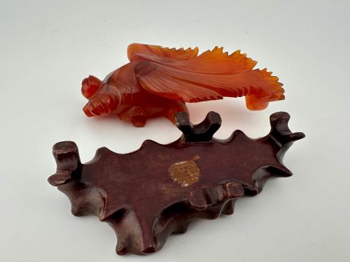 fig 6. A translucent terracotta orange carnelian agate sculpture of a fantail goldfish positioned on a carved dark brown hardwood stand.