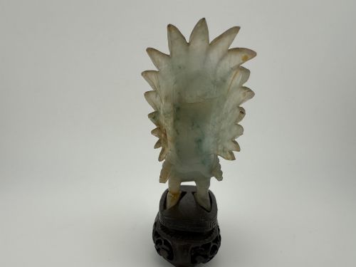 fig 3. A hand-carved pale green jade sculpture of a cockerel with fan-shaped tail feathers, displayed on a dark carved hardwood base.