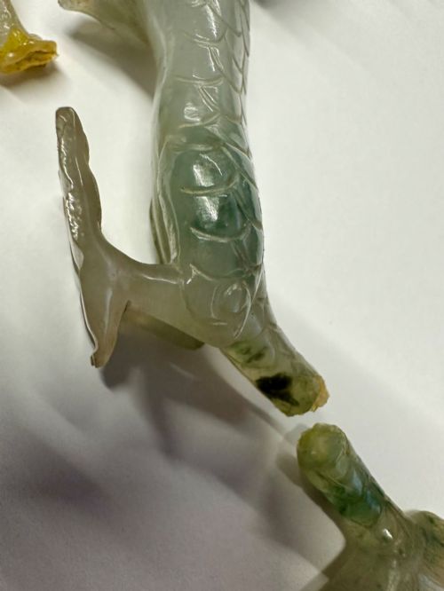 fig 3. A carved pale green jade dragon sculpture shown alongside a dark pierced hardwood display stand.