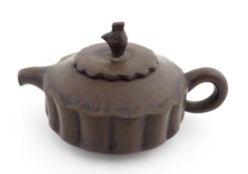 fig 2. A small dark brown unglazed ceramic teapot featuring a lobed body and a bird-shaped finial on the lid.