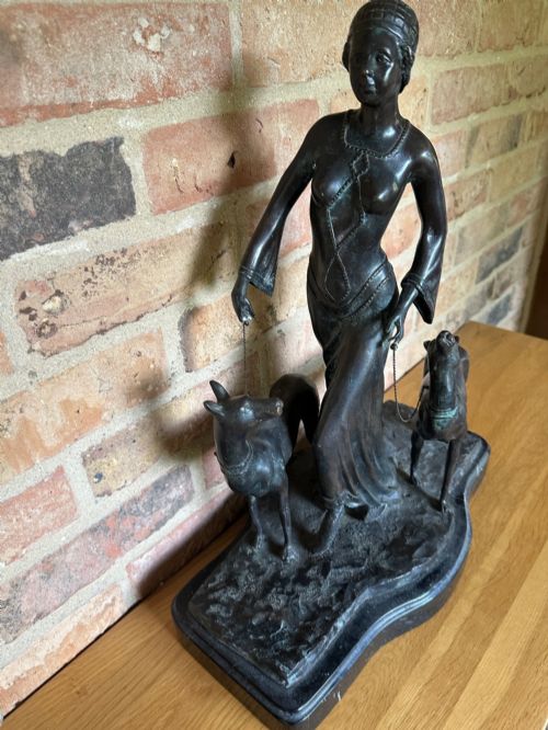 fig 7. A dark bronze Art Deco sculpture depicting a stylised woman walking two greyhounds on thin chains, set on a dark polished marble base.
