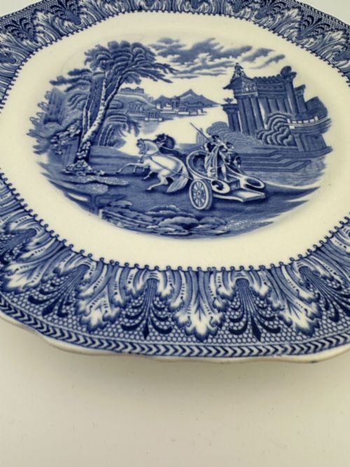 fig 3. An octagonal-edged blue and white transferware plate featuring a central classical chariot scene surrounded by an ornate feather-patterned border.