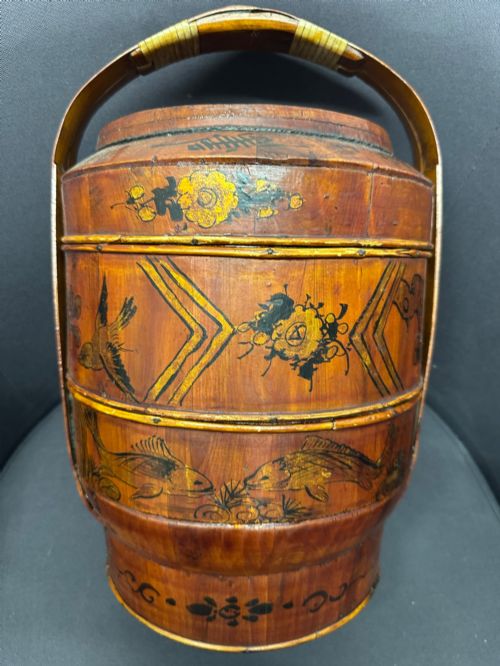 fig 6. A three-tiered late 19th-century Chinese bamboo and wood food carrier with an arched handle, featuring hand-painted yellow flowers, birds, and goldfish against a warm brown lacquer finish.