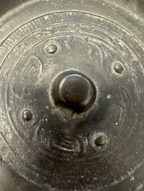 fig 3. A circular ancient bronze mirror back featuring a prominent central knob, raised concentric circular borders, and stylized dragon motifs in low relief.