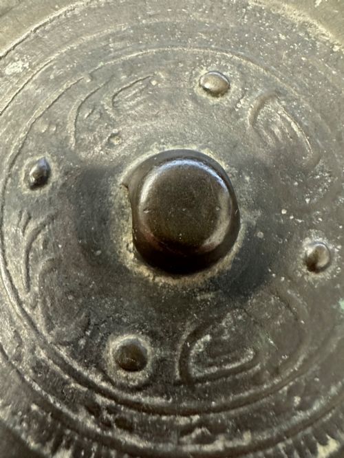 fig 5. A circular ancient bronze mirror back featuring a prominent central knob, raised concentric circular borders, and stylized dragon motifs in low relief.