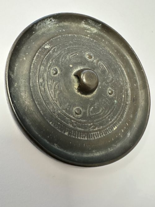 fig 6. A circular ancient bronze mirror back featuring a prominent central knob, raised concentric circular borders, and stylized dragon motifs in low relief.