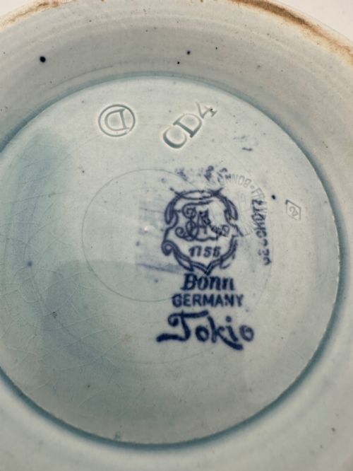 fig 2. A deep circular footed earthenware bowl decorated with blue and white floral and landscape transferware patterns with a brown rim.