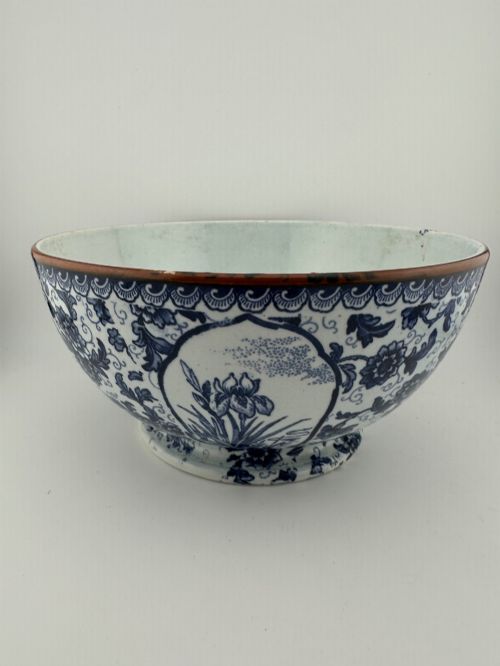 fig 3. A deep circular footed earthenware bowl decorated with blue and white floral and landscape transferware patterns with a brown rim.