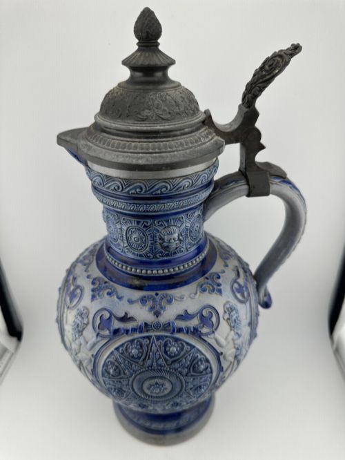 fig 5. A blue and grey salt-glazed stoneware jug featuring relief-moulded geometric patterns, mask motifs, and a hinged pewter lid.