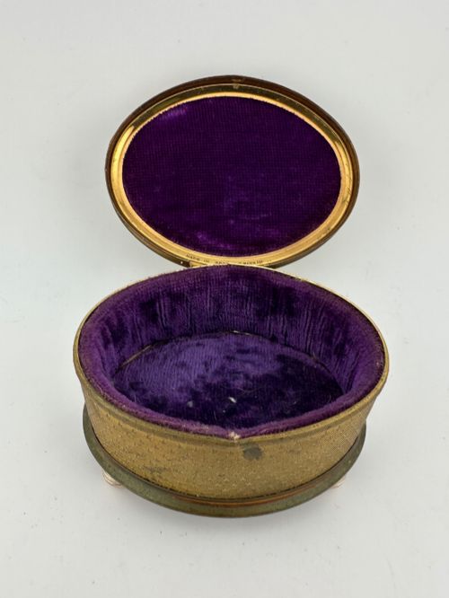 fig 1. An oval vintage metal trinket box featuring a printed floral motif on the lid, star-patterned side panels, small rounded feet, and a velvet lining.