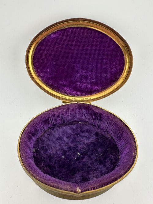 fig 2. An oval vintage metal trinket box featuring a printed floral motif on the lid, star-patterned side panels, small rounded feet, and a velvet lining.