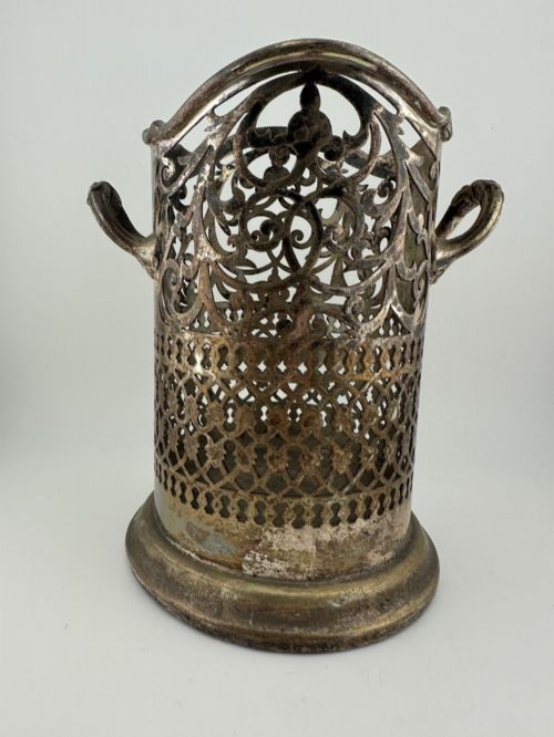fig 2. An antique silver-plated cylindrical wine bottle holder featuring pierced scroll fretwork, two side handles, and a flared circular base.
