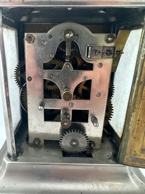 fig 7. An Edwardian carriage clock with a silvered metal casing, brass carrying handle, and engraved brass mask around a white enamel dial.