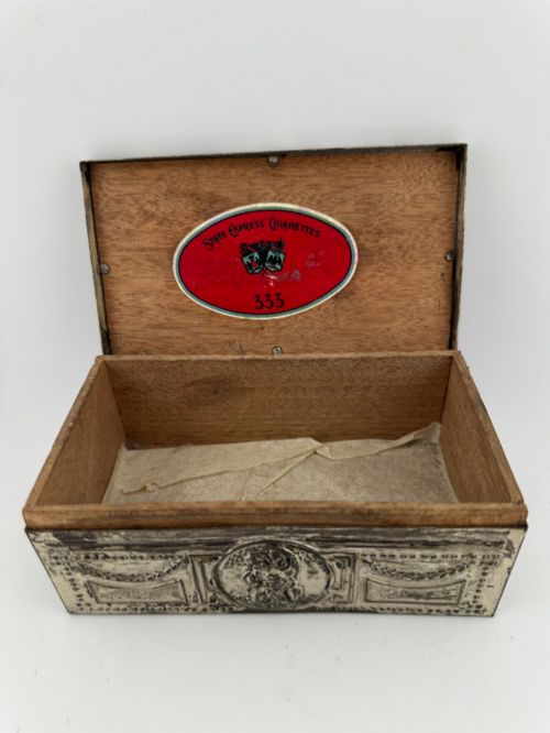 fig 2. A rectangular silver-grey metal box featuring embossed neoclassical cherub medallions and relief swags across its hinged lid and sides.