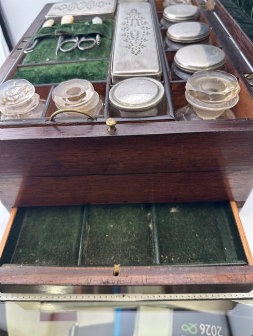 fig 2. An open Victorian rosewood vanity box featuring a ruched green velvet lid lining, fitted interior compartments with silver-capped glass bottles, and a mother-of-pearl escutcheon.