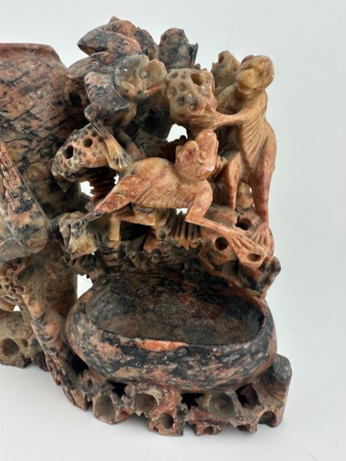 fig 2. A Qing dynasty Chinese soapstone carving depicting a small vase, a shallow brush washer basin, and carved birds among naturalistic floral motifs in mottled red, grey, and cream stone.
